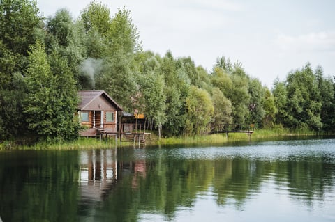 Quaint wooden house on the edge of a beautiful lake surrounded by tall trees and lush greenery